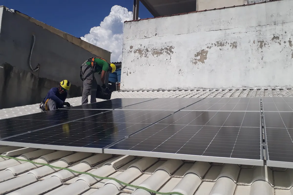 Dois técnicos fixando módulos sobre telha cerâmica branca